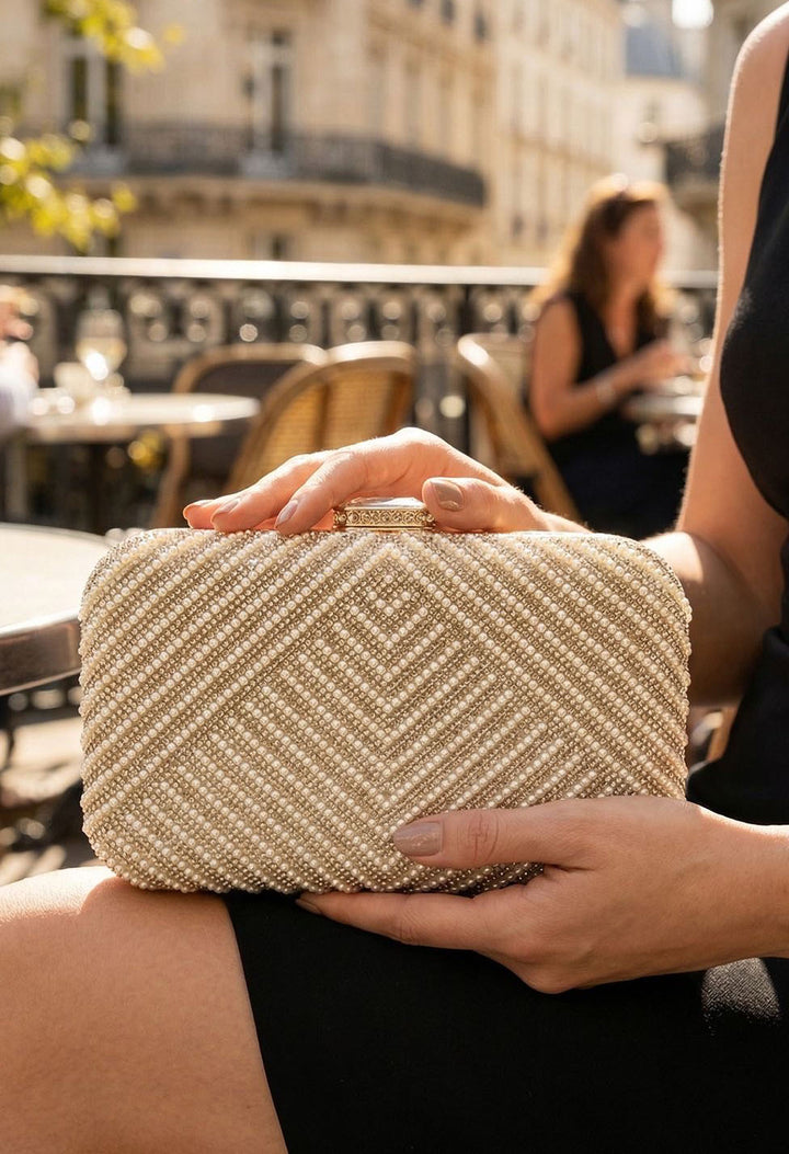 Person holding a gold clutch bag outdoors with blurred background