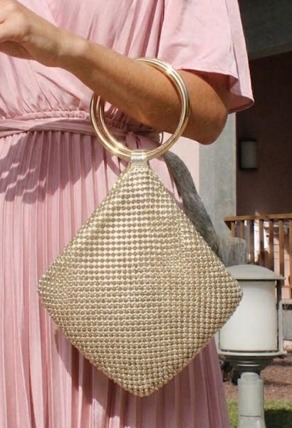 Gold beaded handbag held by a person wearing a pink dress outdoors.