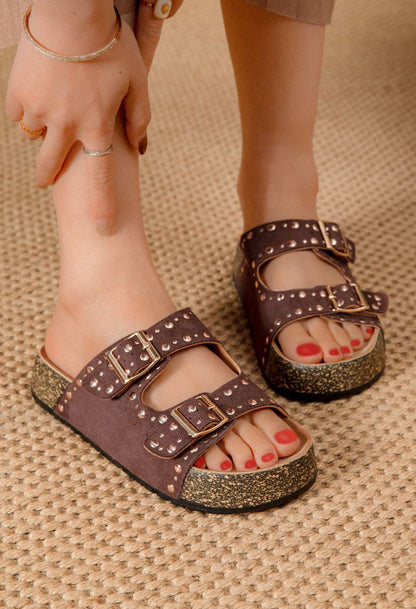 Brown sandals with glittery soles worn by a person on a textured surface