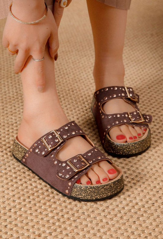 Person wearing black sandals with gold glittery soles on a textured surface