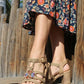 Person wearing a floral dress and beige sandals with embellishments on a wooden deck.