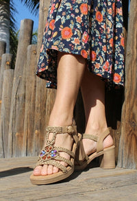 Person wearing a floral dress and beige sandals with embellishments on a wooden deck.