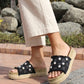 Person wearing black sandals with floral patterns on a stone path with rocks and plants in the background