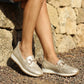 Person wearing silver loafers standing on a stone path with a stone wall background