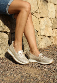Person wearing silver loafers standing on a stone path with a stone wall background