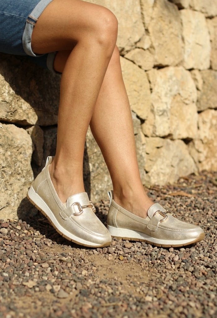 Person wearing silver loafers standing on a stone path with a stone wall background