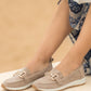 Beige loafers worn by a person sitting on a wooden floor with a beige background