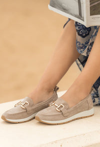 Beige loafers worn by a person sitting on a wooden floor with a beige background