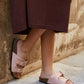 Person wearing pink sandals with brown soles against a stone wall.