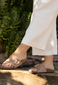 Person wearing taupe sandals with a blurred green background