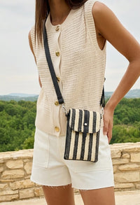 Person wearing a beige sleeveless top and shorts with a black and white striped crossbody bag, standing outdoors.