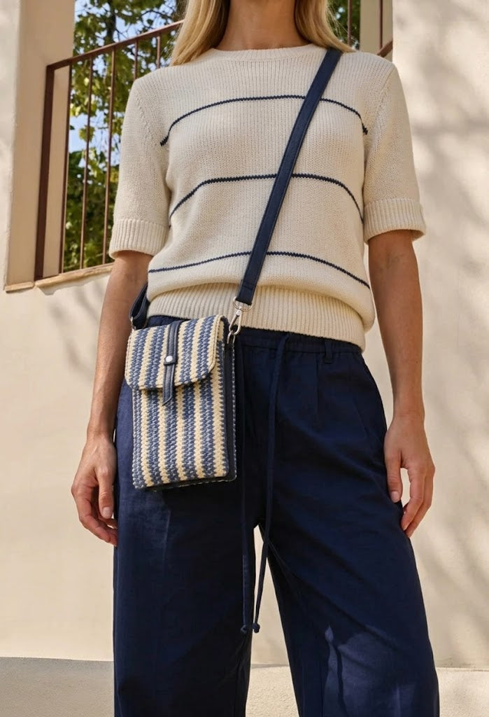 Person wearing a striped sweater and holding a striped handbag outdoors.