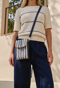 Person wearing a striped sweater and holding a striped handbag outdoors.