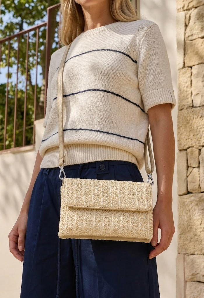 Woman wearing a cream sweater with navy stripes and holding a woven beige handbag.