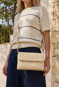 Woman wearing a cream sweater with navy stripes and holding a woven beige handbag.