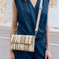 Person wearing a blue sleeveless top and pants with a beige woven handbag.
