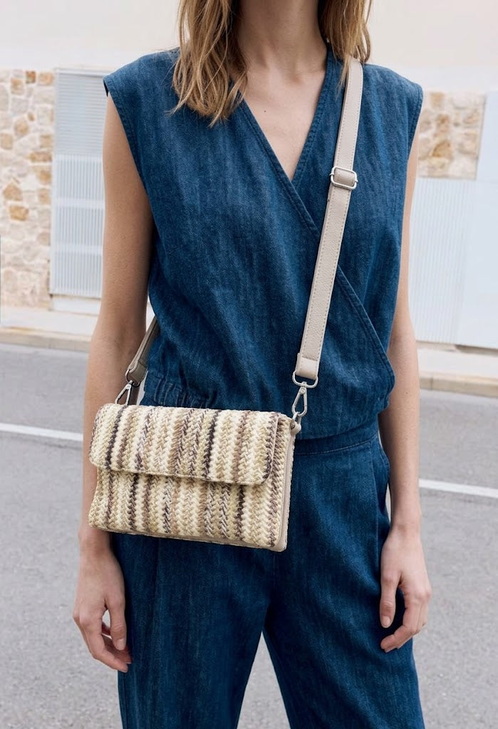 Person wearing a blue sleeveless top and pants with a beige woven handbag.