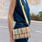 Person wearing a blue sleeveless top and blue pants with a colorful striped handbag on a street.