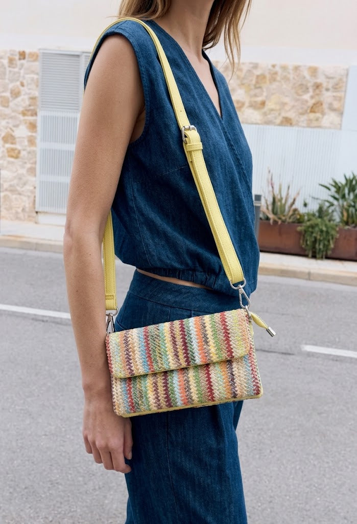 Person wearing a blue sleeveless top and blue pants with a colorful striped handbag on a street.