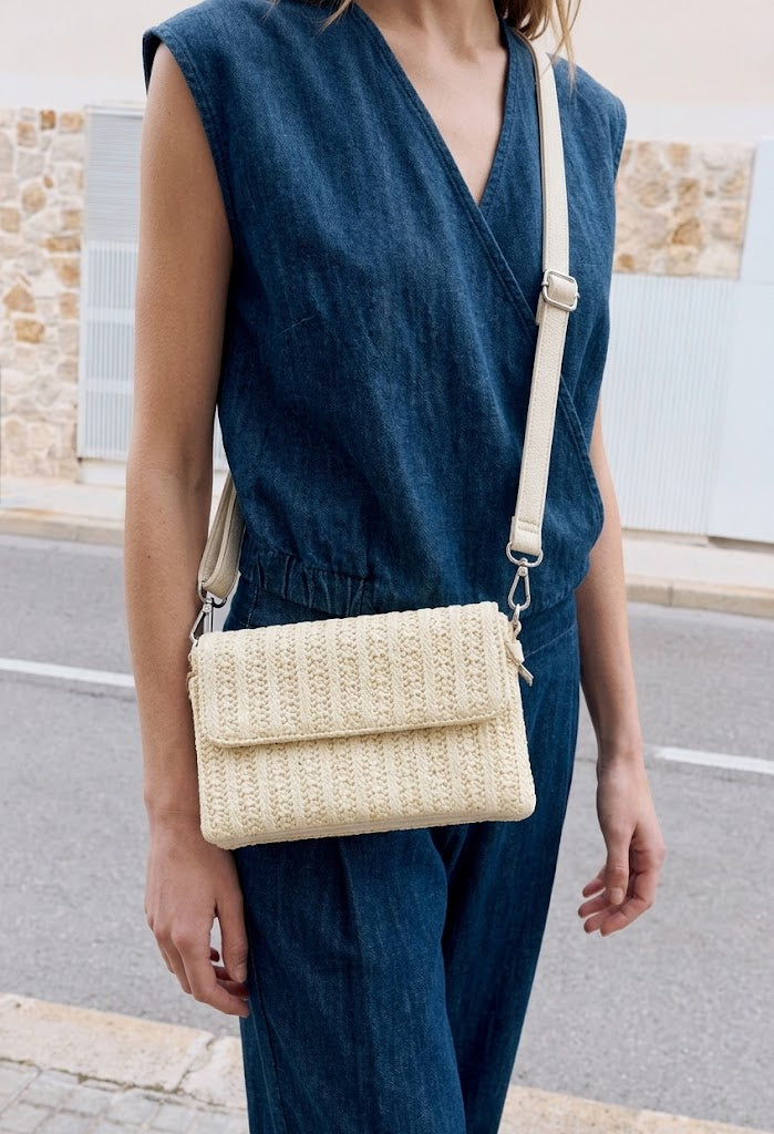 Person wearing a blue sleeveless top and pants with a beige woven handbag on a street.