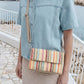 Person holding a colorful striped handbag with a scenic background