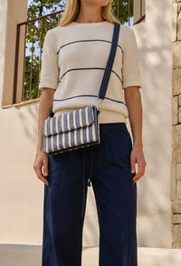 Person wearing a striped sweater and holding a striped handbag outdoors.