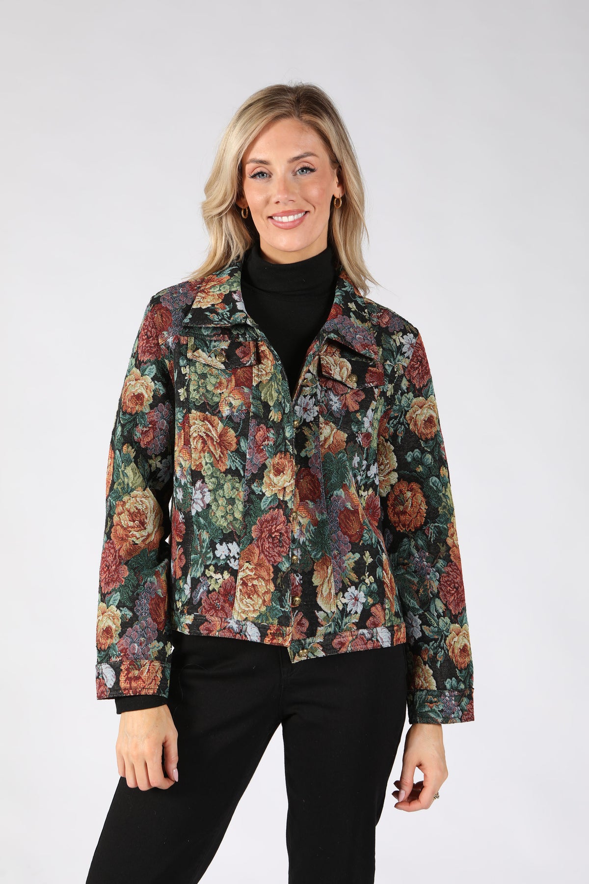 A woman modeling a long-sleeve floral print jacket over a black turtleneck and black pants.