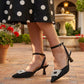 Person wearing black high-heeled shoes with embellishments in an outdoor setting.
