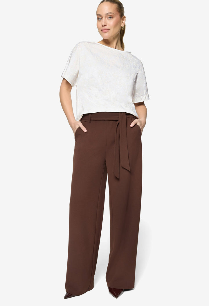 Woman wearing a white top and brown wide-leg pants on a white background