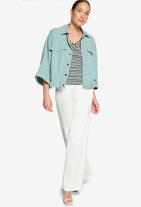 Woman wearing a light blue denim jacket, striped shirt, and white pants on a white background