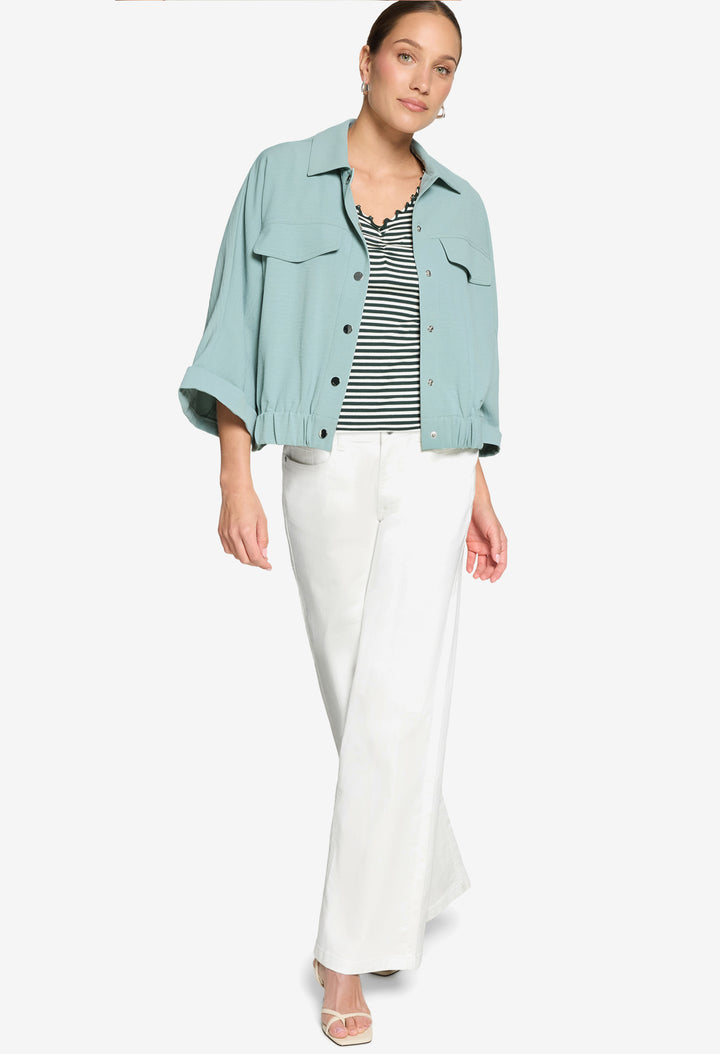 Woman wearing a light blue denim jacket, striped shirt, and white pants on a white background