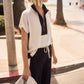 Woman wearing a white and black outfit with sunglasses, standing on a sidewalk.