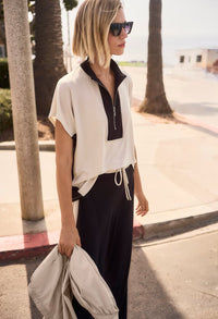 Woman wearing a white and black outfit with sunglasses, standing on a sidewalk.