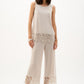 Woman wearing a white sleeveless top and pants with lace details on a white background