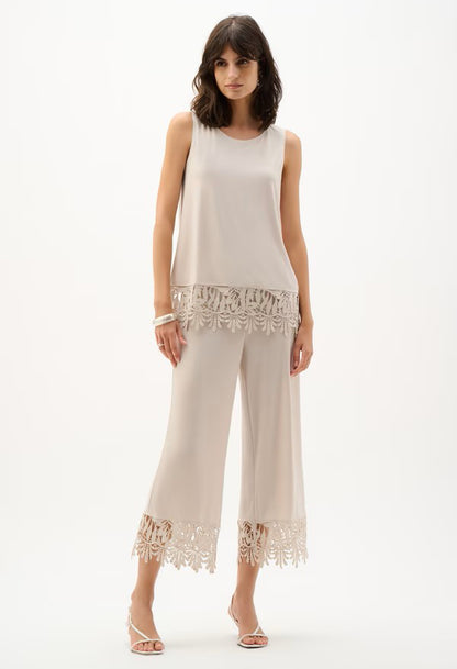 Woman wearing a white sleeveless top and pants with lace details on a white background