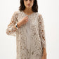 Woman wearing a beige lace jacket over a white top and pants on a white background
