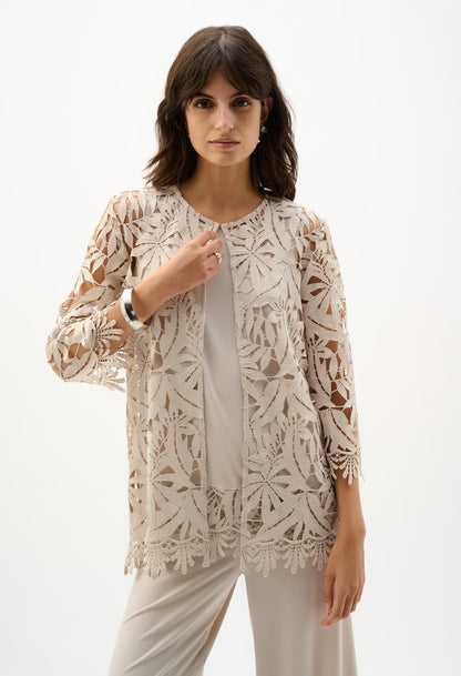 Woman wearing a beige lace jacket over a white top and pants on a white background