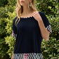 Woman wearing a navy blue top with colorful patterns in front of green foliage