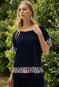 Woman wearing a navy blue top with colorful patterns in front of green foliage