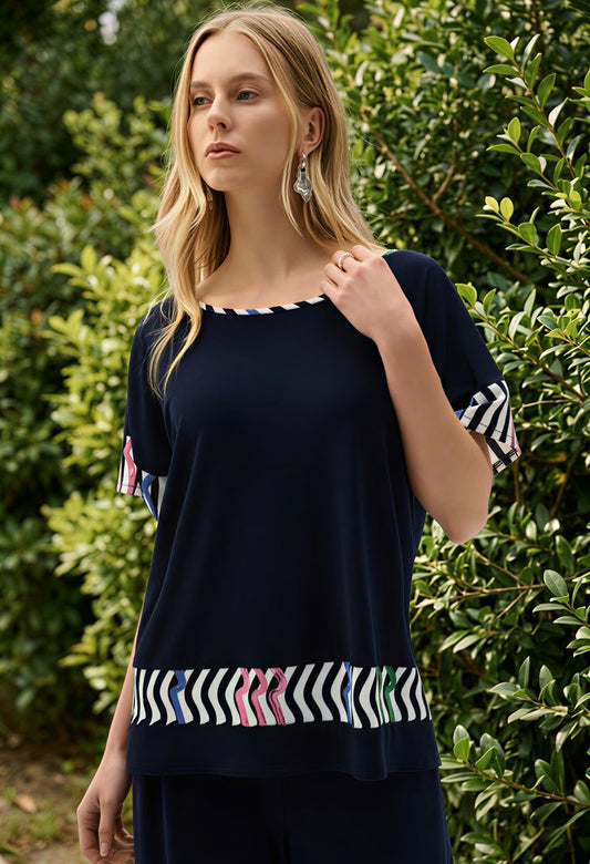 Woman wearing a navy blue top with colorful patterns in front of green foliage