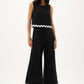 Woman wearing a black sleeveless top and wide-leg pants with white trim on a white background