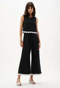 Woman wearing a black sleeveless top and wide-leg pants with white trim on a white background