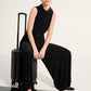 Woman in a black outfit sitting on a black suitcase against a white background