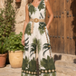 Woman wearing a sleeveless jumpsuit with a palm tree pattern in front of a wooden door.