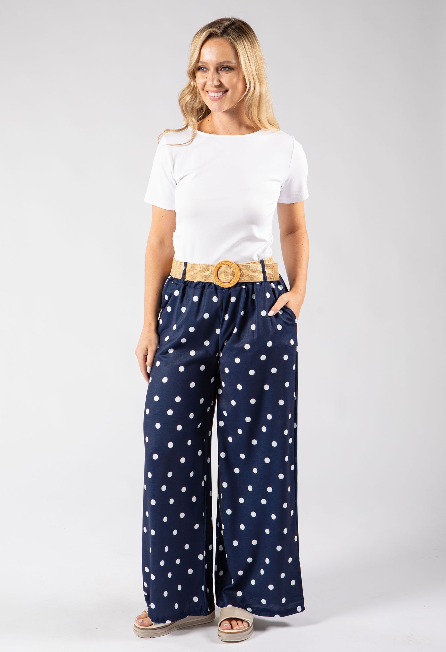Woman wearing a white t-shirt and navy polka dot pants on a white background