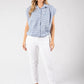 Woman wearing a blue checkered shirt and white pants on a gray background