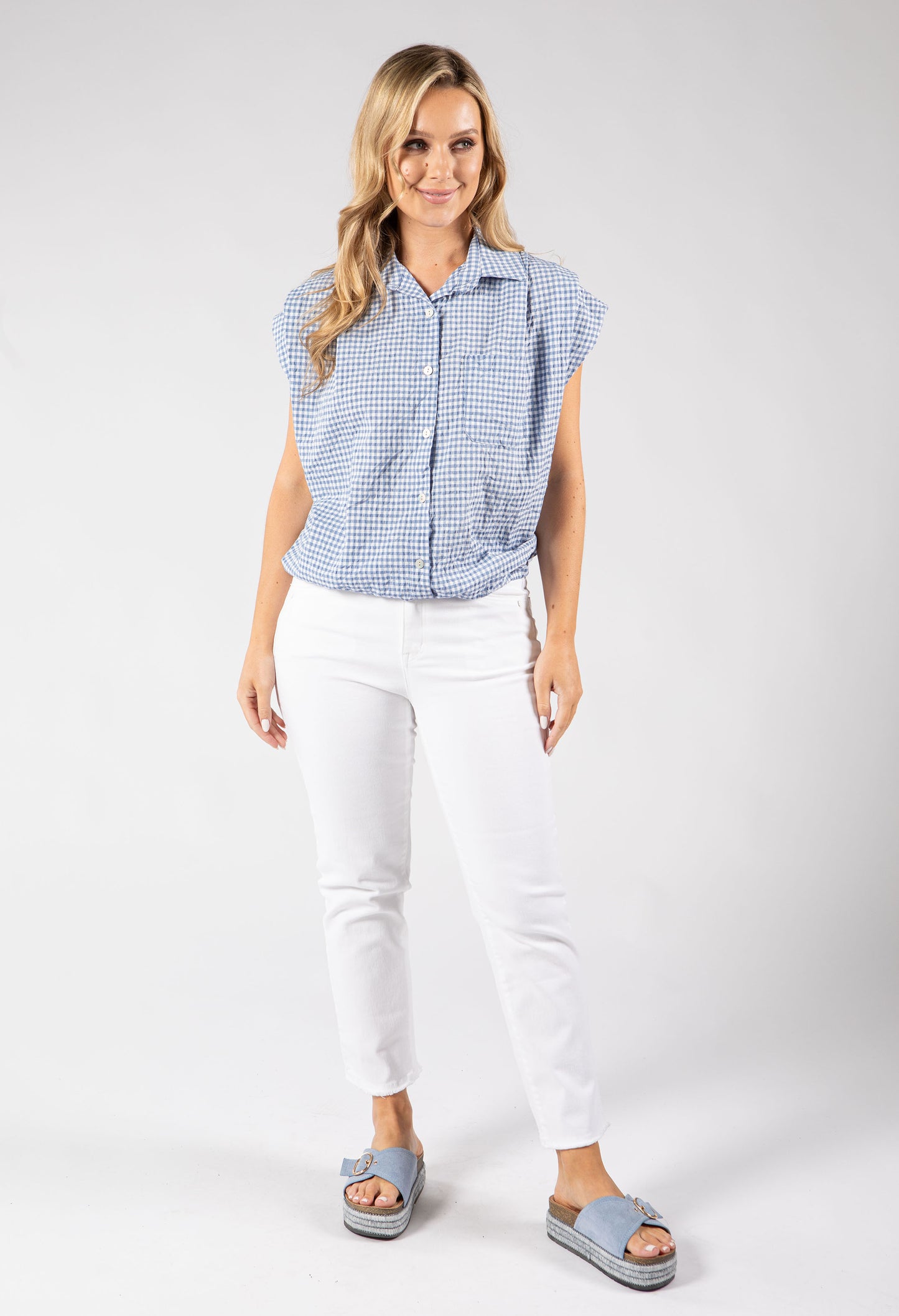Woman wearing a blue checkered shirt and white pants on a gray background