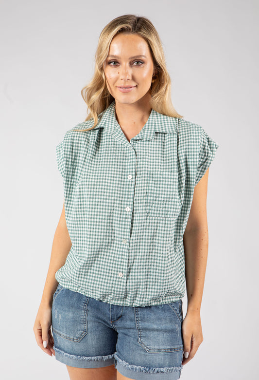 Woman wearing a blue checkered shirt and white pants on a gray background