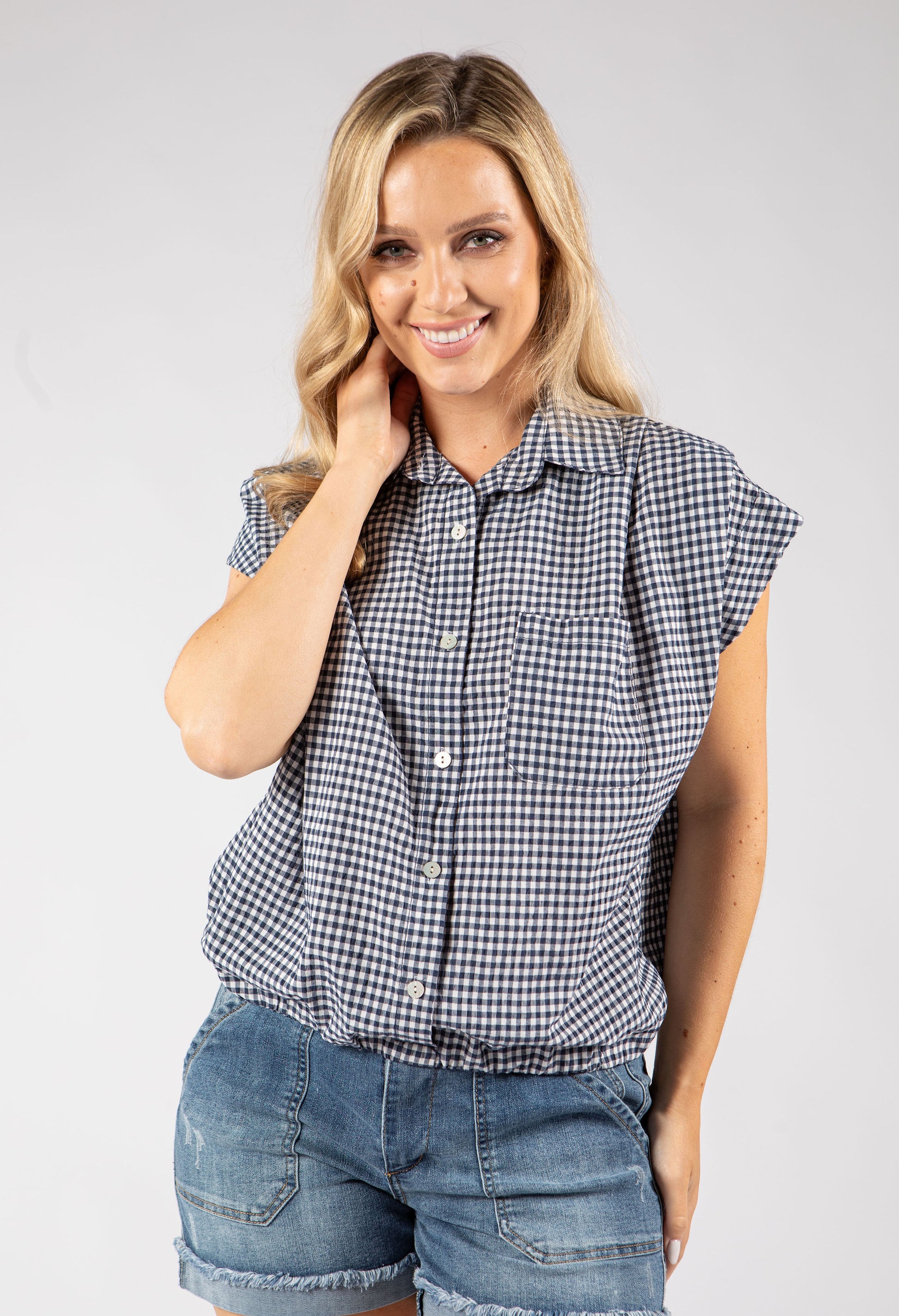 Woman wearing a checkered shirt and denim shorts on a plain background