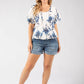 Woman wearing a floral top and denim shorts on a white background